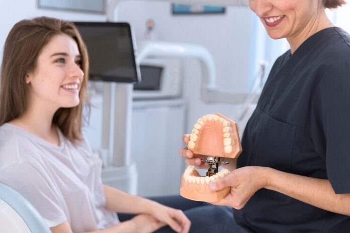 dentist-showing-teeth-model-smiling-patient_23-2147879174